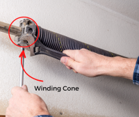 Person's hands adjusting a winding cone on a garage door torsion spring, which is part of the mechanism used to balance and lift the garage door.