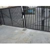 Black metal swing gate that is partially open in San Diego. The design features vertical bars with a few diagonal braces for added support. The gate's structure is affixed to a concrete base, and there is a metal plate on the ground indicating the gate's pivot point or closure mechanism.
