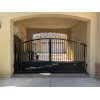 Wrought iron swing gate with vertical spindles and scrolled top.