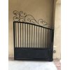 Black pedestrian swing gate. Vertical spindles with elaborate scroll work across the top.