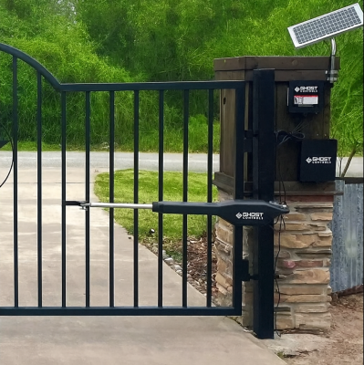 A black wrought iron automatic swing gate with vertical bars is installed on a stone pillar and equipped with a solar powered opener system. 