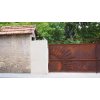 Rust stained sliding entrance gate with intricate sunshine design and rounded top at a luxurious neighborhood in San Diego.