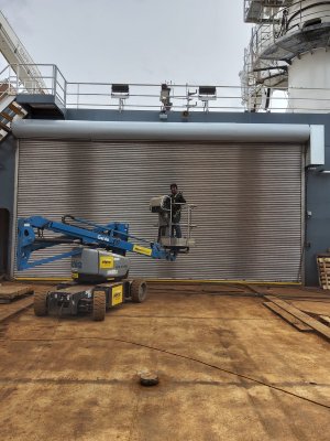 A technician operates a  boom lift in front of a large commercial roll-up door at an industrial facility.