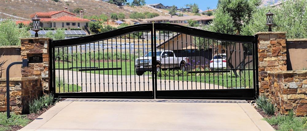 Black custom wrought-iron driveway gate with stone pillars at a San Diego home