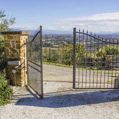 An open wrought iron gate attached to a stone pillar leads to a gravel driveway near San Diego